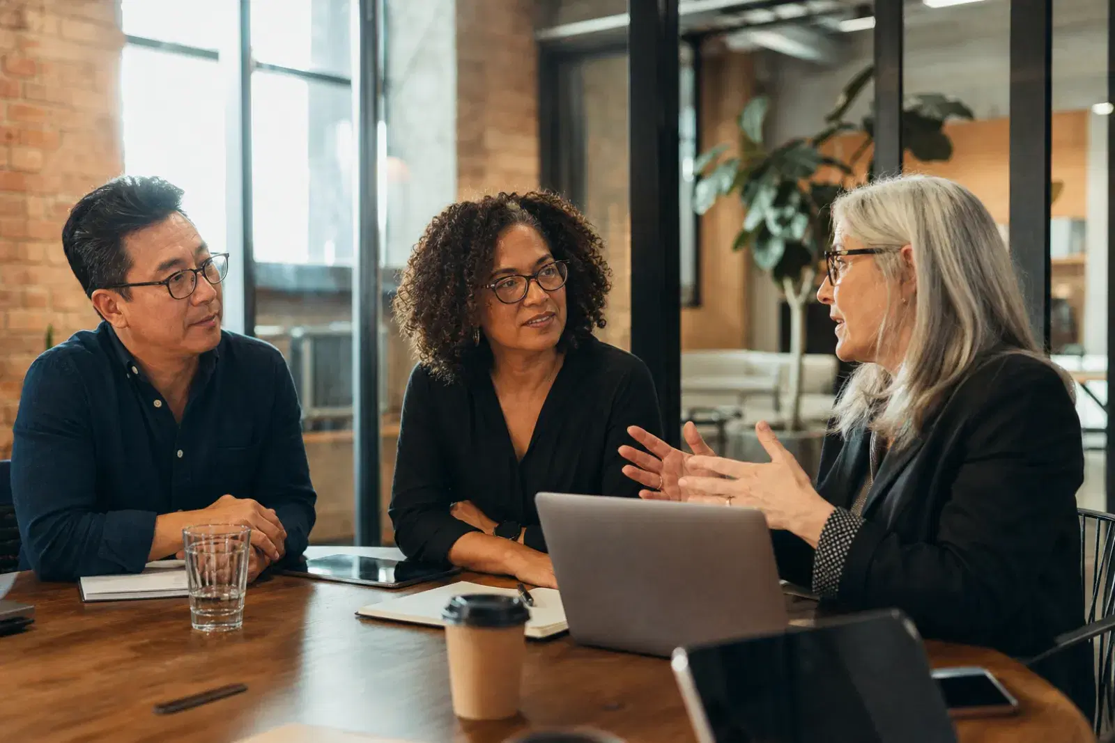 An HR leader presenting a development plan to two colleagues in a glass-walled meeting room.