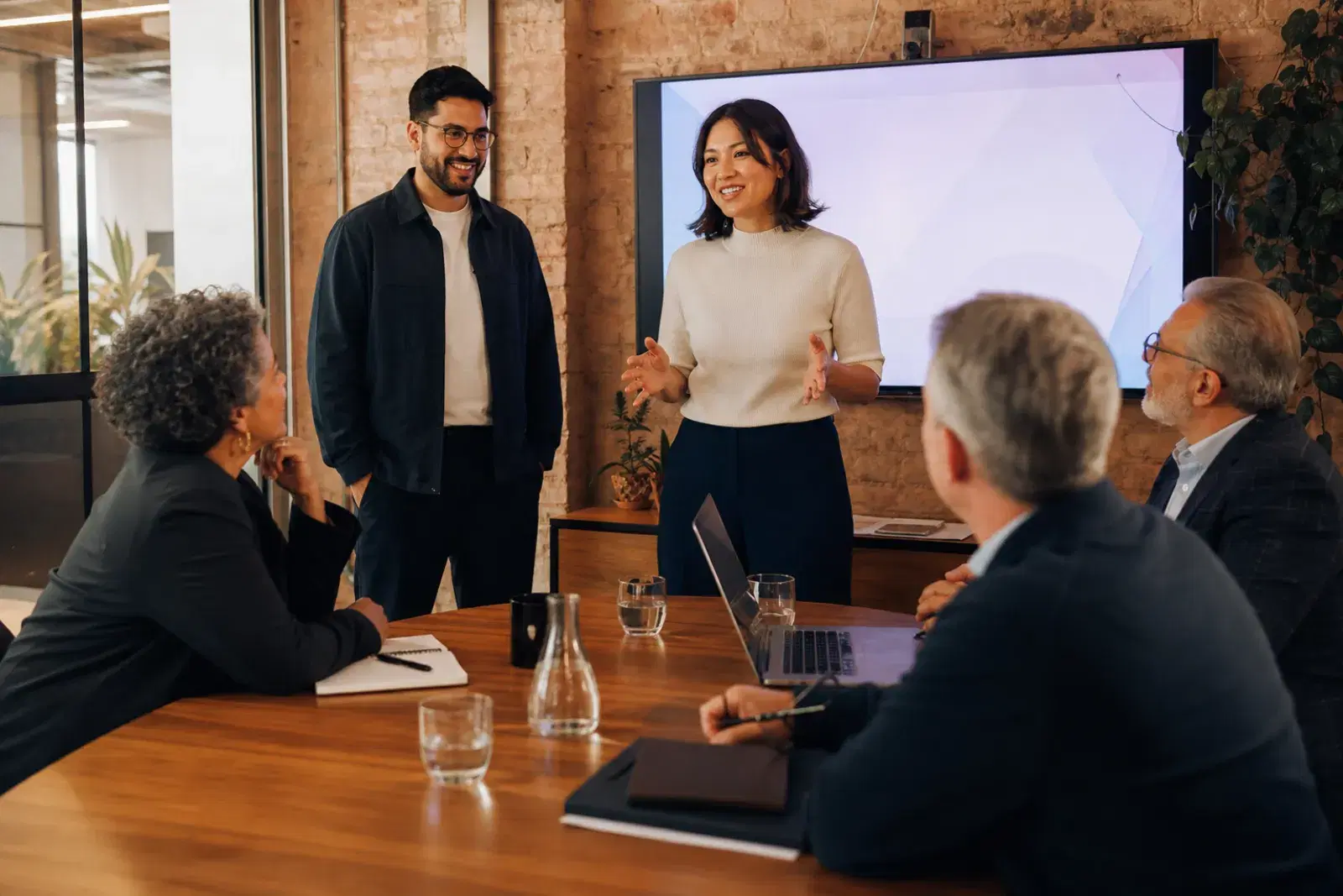 Two startup founders delivering a pitch to three seated investors in a small meeting room.