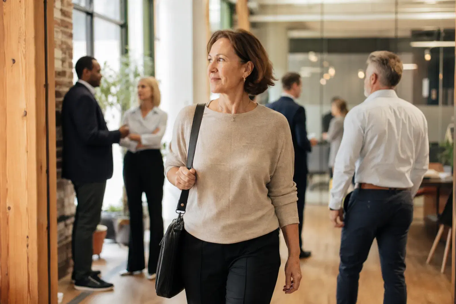 A consultant walking through a bright office lobby with a laptop bag over her shoulder