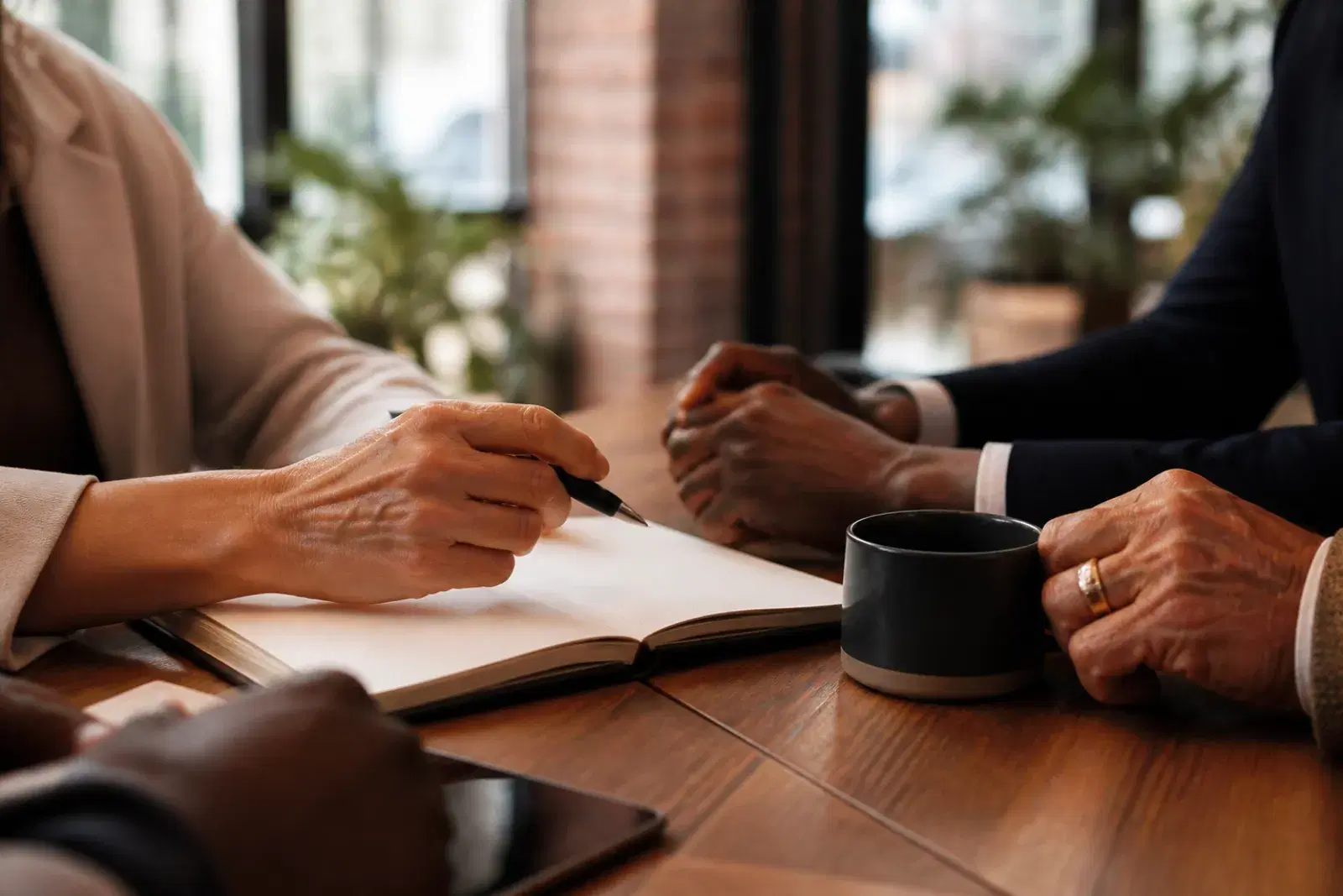 Hands resting near an open notebook and a coffee cup on a boardroom table.